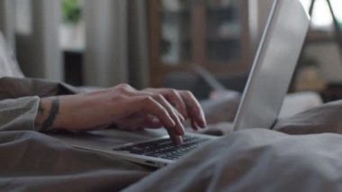 Yavaş çekimde, tanımlanamayan dövmeli erkek elleri dizüstü bilgisayarda yazarak kilitlenirken evden çalışıyor.