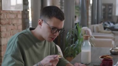 Modern çatı katında mısır gevreği yerken, adamın mutfakta dizüstü bilgisayarla oturduğunu gösteren yavaş çekim görüntüleri.