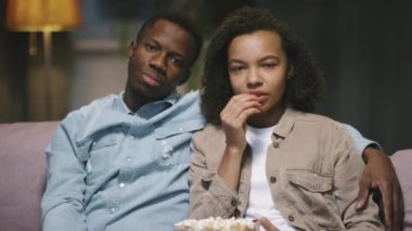 Televizyonda ilginç filmler izleyen, patlamış mısır yiyen, geceleri oturma odasındaki kanepede oturan Afrikalı Amerikalı genç çiftin yavaş çekim görüntüsü.