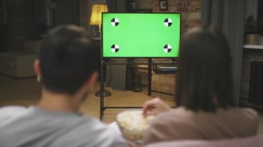 Televizyonun karşısında oturan, futbol maçının tadını çıkaran, patlamış mısır yiyen çiftin dikiz görüntüsü.