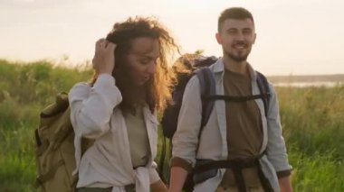 Genç adam ve kadın aşıklar hafta sonunu doğada sırt çantalarıyla yürüyüş yaparak, el ele tutuşarak ve sohbet ederek geçiriyorlar.