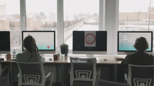 Pan拍摄的年轻男女呼叫中心特工坐在电脑前 透过全景窗和社交场合的距离 与客户进行音频通话 — 图库视频影像
