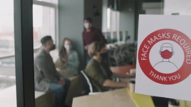 Yüz Maskeleri 'nin yavaşlaması için ofiste cam duvarda tabela gerekliydi. Yüz maskeli iş adamları içeride çalışıyor.