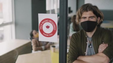 Yüz maskeli genç erkek ofis çalışanının PAN portresi. Cam duvarın yanında poz veriyor. Yüz maskesi gerekiyor.