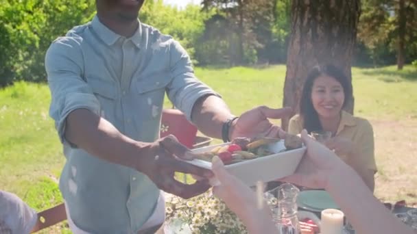 夏の日に都市公園で昼食を共にした多民族の男性と女性の手によるスローモーションズームアウト — ストック動画
