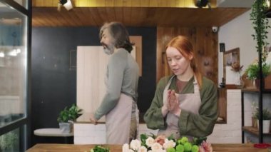 Çiçekçi dükkanındaki en iyi çiçekleri seçen iki işçinin küçük, rahat çiçekçi dükkanındaki tezgahta duran güzel buketi düzenlediği orta boy bir fotoğraf.