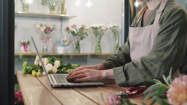 工作期间站在笔记本电脑柜台旁打字的无法辨认的女性花店店员的中间片段 — 图库视频影像