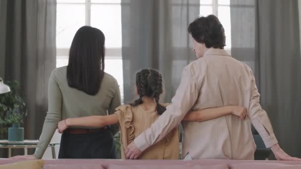 一列に並んだ三世代の女三人が 居間の窓から抱き合って笑っている姿を 後景のスローモーメディアで映し出す — ストック動画