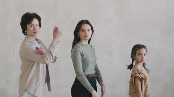 スローモーション メディア スタジオ ポートレートの3人の多世代女性が白い背景でスーパーヒーローのポーズに立ち 片手を腕に置き カメラを真剣に見る — ストック動画