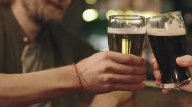 Slow-motion close-up of unrecognizable male friends toasting beer glasses at bar