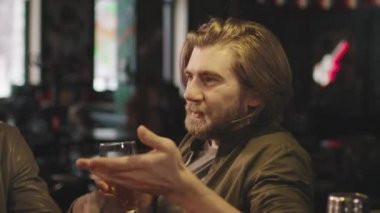Kafkas sakallı genç bir adam barda oturmuş arkadaşlarıyla konuşuyor ve geceleri bira içiyor.