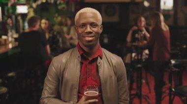 Orta boy portre çiziyor. Siyah saçlı, gülümseyen Afrikalı Amerikalı bir adam. Elinde bir bardak bira, akşam arkadaşlarıyla barda takılıyor.