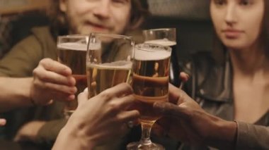 Orta boy, akşamları barda oturmuş bira bardaklarını yudumlayan genç insanlarla yakın çekim.