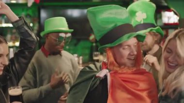 St. Patrick Günü 'nde İrlanda barında bira içip dans eden enerjik çok ırklı genç arkadaşlarla orta boy yakın çekim.