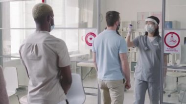 Çok nesilli çeşitli hastaların yavaş çekimleri, kadın hemşire tarafından kontaktsız kızılötesi termometre kullanılarak vücut ısıları ölçülüyor.