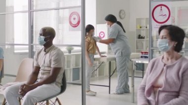Diğer hastalar modern klinikte kuyrukta beklerken küçük kız ve yetişkin adamın kovid 19 aşısına maruz kalışının orta ölçekli görüntüleri.