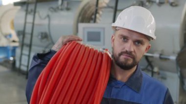  Ciddi bir erkek bitki işçisinin portresi, kasketli ve üniformalı, elinde küçük çaplı HDPE borularıyla kameraya bakıyor.
