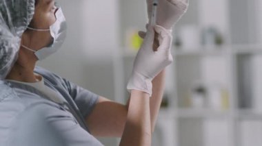 Korunaklı maske ve eldivenli kadın doktorun yavaş çekimde Coronavirus aşısı olmadan önce şırıngayı aşıyla doldurması.