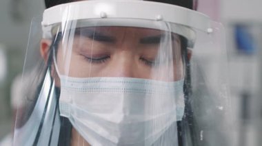 Kadın melez doktorun koruyucu yüz kalkanı takmış kameraya bakarken yavaş çekimde çekilmiş portresi.