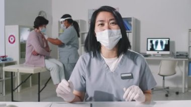 Yüzü maskeli kadın melez kadının belden aşağısı kameraya bakıp online video görüşmesi yaparken, son sınıf öğrencisi kadının hastane koltuğunda otururken kovid aşısı olması.