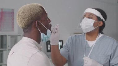 Ağır çekimde, Coronavirus testi için genç Afrikalı Amerikalı bir adamın boğazından örnek alırken çekilmiş.