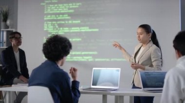 Ekran projektörüne atıfta bulunarak ders ve sınıf arkadaşlarına kodlama bilgileriyle dolu bilgisayar programlama sorunu hakkında rapor hazırlayan genç kız