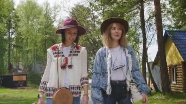 Boho tarzı giyinmiş, ağaçların arasında yürüyen, konuşan ve müzik festivaline gülümseyen çekici genç kadınların ön-görüntüsü.