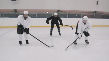 Üniformalı ve kasklı erkek hokey oyuncularının boş buz arenasında durup kameraya baktıkları yavaş çekim.
