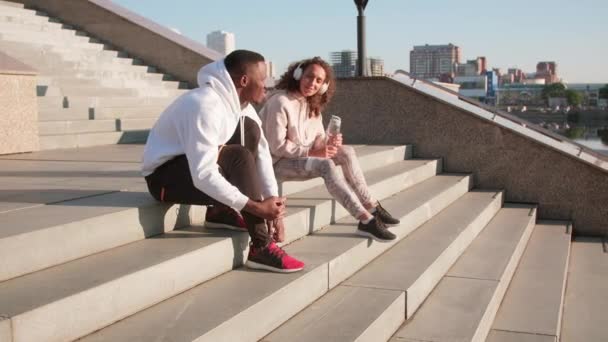 在阳光灿烂的早晨和女友一起边锻炼边聊天边一起享受训练的非洲裔美国男人坐在户外楼梯上的全景照片 — 图库视频影像