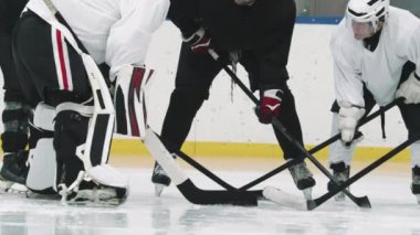 Profesyonel hokey koçunun kırmızı kasklı ve genç oyuncuların antrenman sırasında buz üzerinde daireler çizerek hokey hileleri ve tekniklerini tartışırken çekimleri.