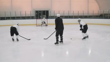 Erkek hokey oyuncularının tam dikiz görüntüsü. Kaleci kapıda dikilirken hokey antrenmanı yapıyorlar.