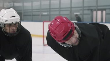 Profesyonel hokey koçunun yavaşlığıyla yakın plan çekimde. Kırmızı kasklı, takım talimatlarını veriyor. Buz arenasında bir arada duruyorlar.