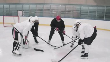 Hokey koçunun oyunculara pozisyonlarını almalarını söyleyip sonra da kapalı buz sahasında oynamaya başladıkları yüksek açılı bir çekim.