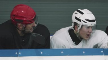 Tribünde oturmuş buz arenasını tartışan kasklı beyaz erkek hokey oyuncularının orta ölçekli yakın çekimi.