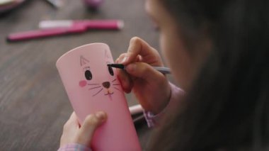 Masada oturan ve kurşun kaleme tavşan surat çizen bir kızın omuz fotoğrafını çek.