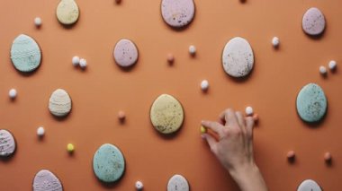 Tanınmayan bir kadının turuncu renkli yüzeye lezzetli Paskalya kurabiyeleriyle boyanmış bıldırcın yumurtası yerleştirdiği düz bir görüntü.