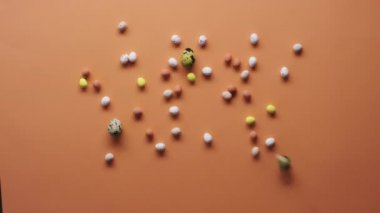 Turuncu yüzeyde boyanmış bıldırcın yumurtalarının ve renkli paskalya şekerlerinin üst görüntüsü.