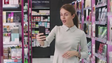 İyi görünümlü bir kadının kozmetik mağazasında ayakta duran akıllı telefon aracılığıyla video konuşması yavaş çekim.