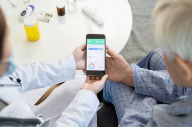 Whitecoat 'taki kadın pratisyen hekimin elleri, uzman erkek hastaların bireysel sağlık programının sonuçlarına bakmak için akıllı telefon kullanıyor.