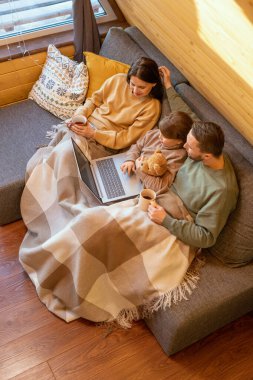 Mutlu, sevecen, süveterli bir aile. Kır evindeki ekoseli kanepenin altında rahatlıyor ve çevrimiçi film seyrediyor.