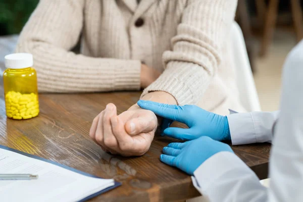全科医生在家中进行体格检查时 按桌子触摸老年病人脉搏时戴手套的手 — 图库照片