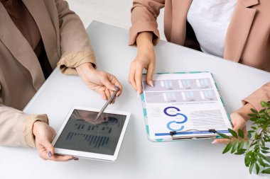 Toplantıda yan yana otururken çizelgeleri ve şemaları analiz eden ve tartışan iki genç iş kadınının elleri