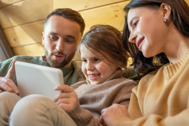 Üç kişilik mutlu genç aile evlerinde rahat rahat oturup tablet ekrana bakarken online film izliyorlar.