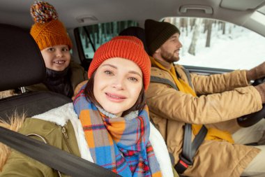 Sıcak kış giysileri içinde mutlu genç bir kadın arabada kocasının yanında otururken selfie çekiyor.