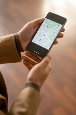 Şehrin çevrimiçi haritasında cadde ya da evi bulmaya çalışırken bej ceketli genç işadamının elleri cep telefonu kullanıyor.