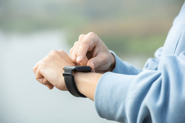 Руки молодой современной спортсменки в синей спортивной одежде, смотрящей на наручные часы перед тренировкой, стоя перед камерой на улице