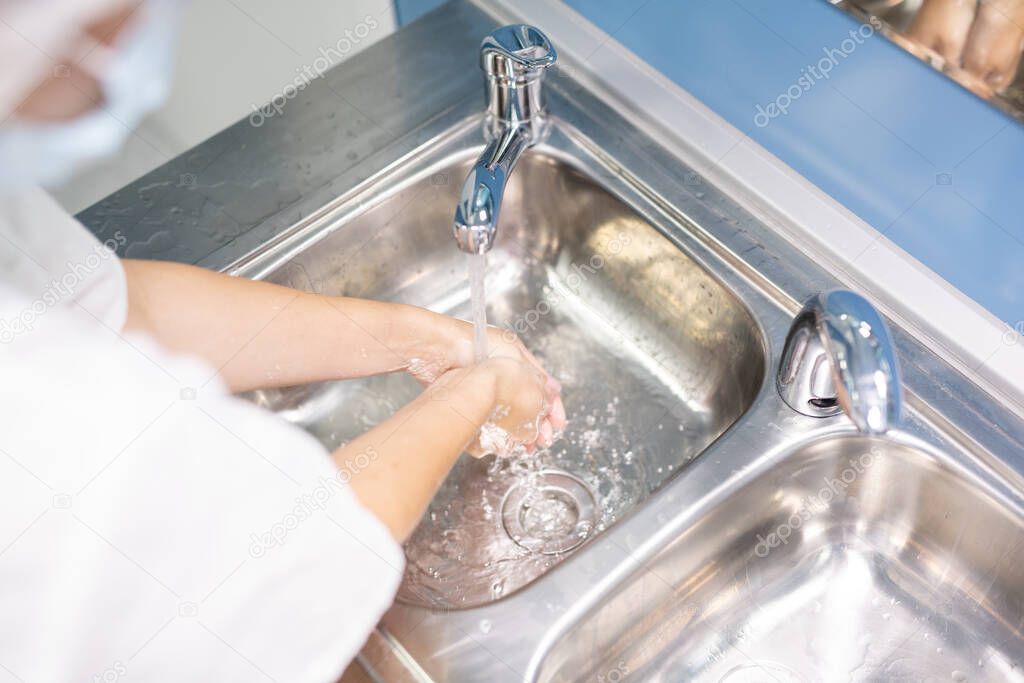 Young assistant, nurse or doctor in white uniform washing hands over one of two metallic sinks before or after medical procedure in clinics
