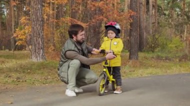 Neşeli sakallı baba, beş yaşındaki şirin oğluna parkta bisiklete binmeyi öğretiyor.