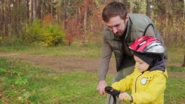 Neşeli babayla yavaş bir yarış. Park yolunda dengeli bisiklet süren sevimli 5 yaşındaki oğluna yardım ediyor.