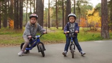 Güneşli bir sonbahar gününde kasklı bisiklette oturan ve parkta kameraya poz veren 5 yaşındaki tatlı bir çocuk ve kızın portre görüntüsü.